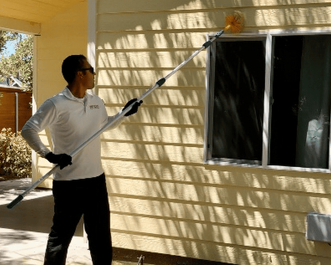 esse Moreno, the owner of Efficient Pest Control, uses a long-reach brush to clean spiderwebs and nests from the exterior of a home in Oxnard, CA